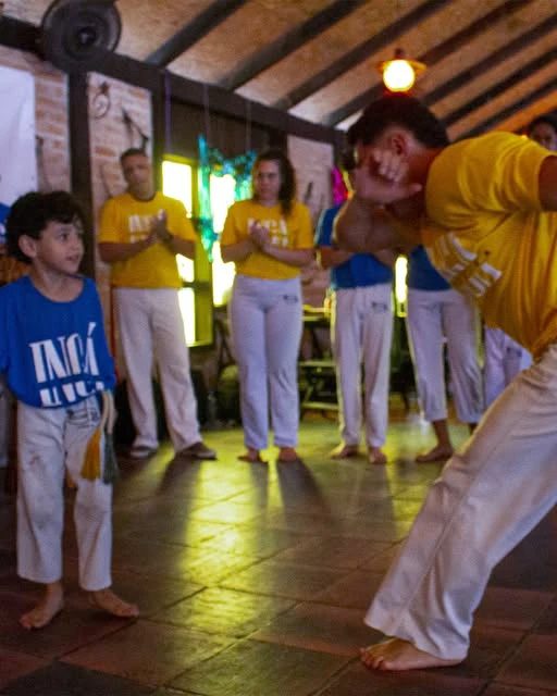 Criança observa o movimento de um adulto na roda de capoeira